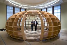 two men standing in front of a large wooden object