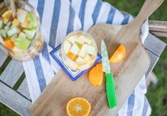 a wooden cutting board topped with sliced oranges next to a bowl of apples and an apple cider