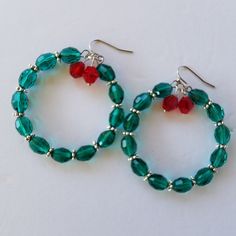 pair of green beaded hoop earrings with red beads on white table top next to each other