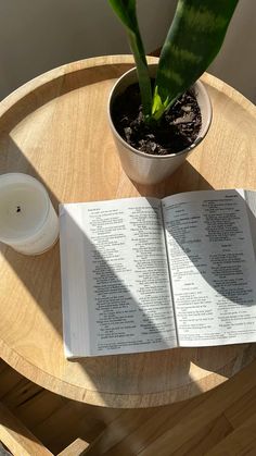 an open book sitting on top of a wooden table next to a potted plant