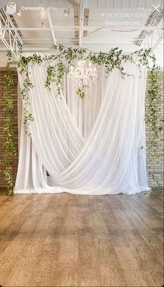 an empty room with white drapes and greenery hanging from the ceiling in front of it