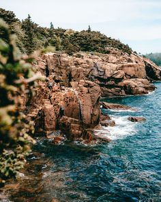 a man standing on top of a rocky cliff next to the ocean with trees in the background