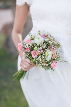 a woman holding a bouquet of flowers in her hand and wearing a white dress with pink roses on it