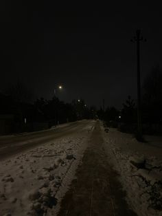 a dark street at night with snow on the ground and light poles in the distance