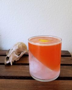 a glass filled with liquid sitting on top of a wooden table next to a skull