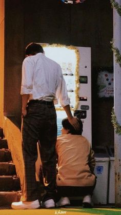 two men sitting on the ground in front of a vending machine