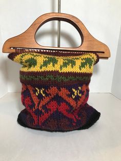 a wooden hanger holding a multicolored knitted purse on top of a white surface