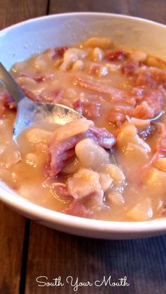 a white bowl filled with pasta and meat next to a spoon on top of a table