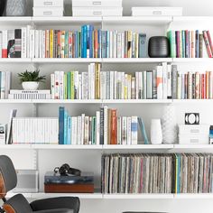 a bookshelf filled with lots of different colored books next to a white chair