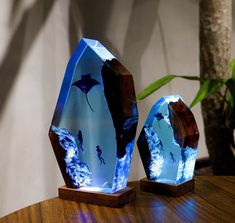 two blue glass sculptures sitting on top of a wooden table next to a potted plant