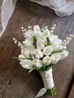 a bouquet of white flowers sitting on top of a wooden floor next to a veil