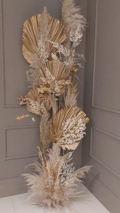 an arrangement of dried flowers in a vase on a white countertop next to a gray wall