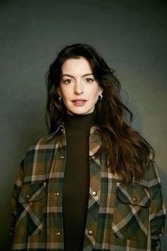 a woman with long dark hair wearing a green plaid jacket and black turtle neck sweater