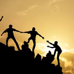 four people are standing on top of a mountain and reaching for the sky with their hands