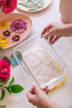 a person is holding a cloth in front of a glass container with flowers on it