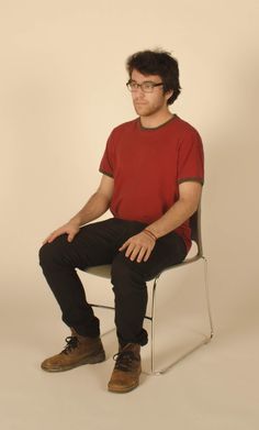 a man sitting in a chair with his legs crossed, wearing glasses and a red shirt