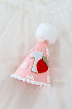 a pink birthday hat with a strawberry on the front and number one on the back