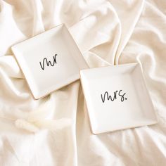 two white plates with the words mrs and mr written on them sitting on a bed