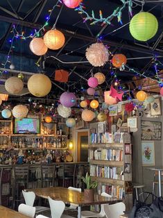 many paper lanterns hang from the ceiling above a table in a room with chairs and bookshelves