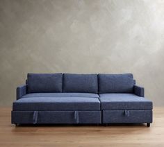 a blue couch sitting on top of a hard wood floor next to a gray wall