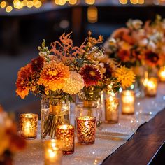 candles are lined up on a table with flowers in vases next to each other