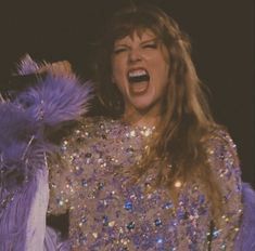 a woman singing into a microphone with purple feathers