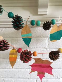 some pine cones and leaves hanging from a string on a brick wall in front of a window