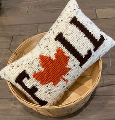 a crocheted pillow with an orange maple leaf on it sitting in a basket