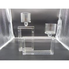 three clear vases sitting on top of each other in a glass box with two lamps