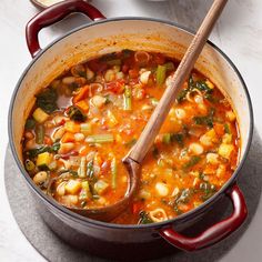 a red pot filled with soup next to a wooden spoon