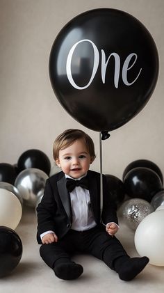 a little boy in a tuxedo holding a balloon with the word one on it