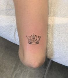 a woman's foot with a small crown tattoo on her left leg, sitting on a bed