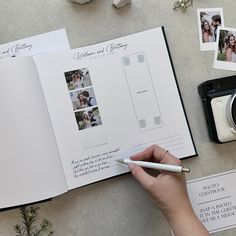 a person holding a pen and looking at an open wedding album with photos on it