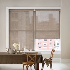 a dining room table with two chairs and a large window covered in roman blind shades