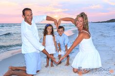 a family on the beach holding hands and making a heart shape in the sand at sunset