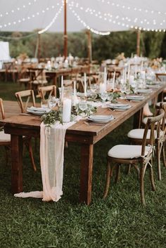 a long wooden table topped with white plates and place settings next to an umbrella covered tent