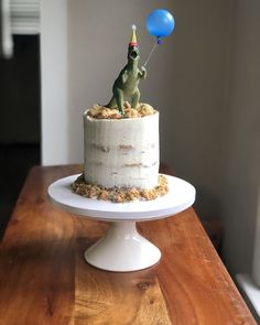 a birthday cake with a frog on top and a blue balloon in the air above it