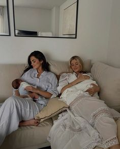 two women are sitting on a couch holding their babies and looking at something in the mirror