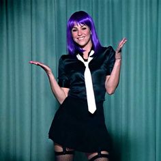 a woman with purple hair wearing a black dress and white tie posing for the camera