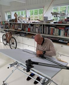 a man working on an object in a room with many bookshelves and bicycles