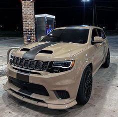 a beige jeep parked in front of a brick building at night with its hood up