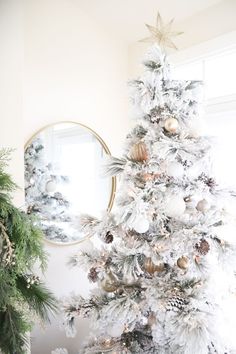 a white christmas tree with gold and silver ornaments on it, in front of a mirror