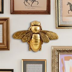 a gold bee mounted on the side of a wall next to framed pictures and paintings