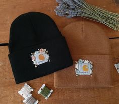 two beanies and pins are sitting on a wooden table next to lavenders,