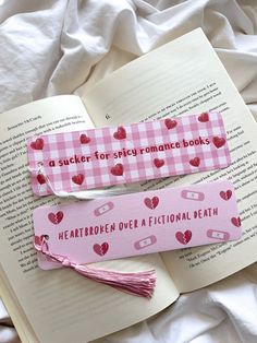 two pink bookmarks with hearts on them are laying next to an open book that says, a sucker for spicy romance books