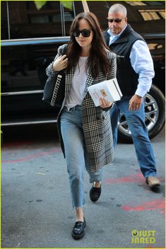 a woman walking down the street while wearing jeans and a blazer with her hand in her pocket