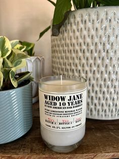 a white candle sitting on top of a wooden table next to a potted plant