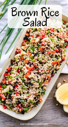 brown rice salad in a white dish with lemons and green onions on the side