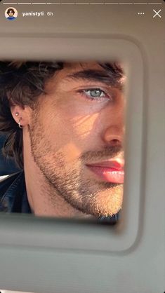 a man with blue eyes looking at himself in the rear seat of a car mirror