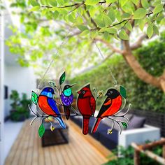 three colorful birds are hanging from a tree in front of a deck with chairs and trees